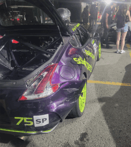 Close-up of a purple Solidxperts Nissan 370Z race car with neon green wheels, showing rear-end damage sustained during the race.